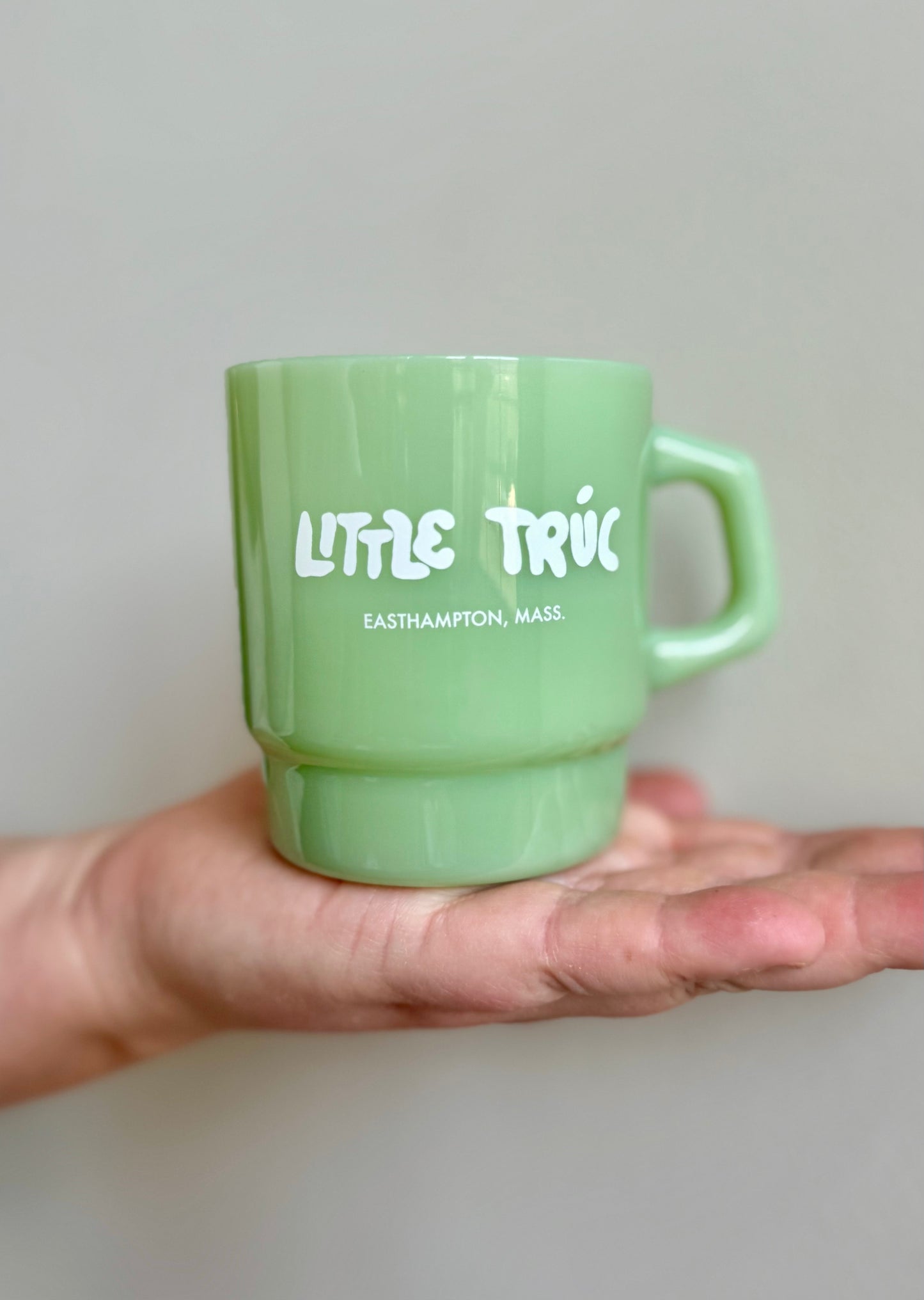 Green mug with 'Little Truc' text held in a hand against a neutral background