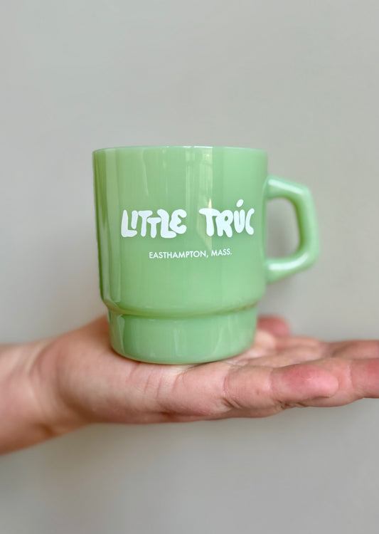 Green mug with 'Little Truc' text held in a hand against a neutral background